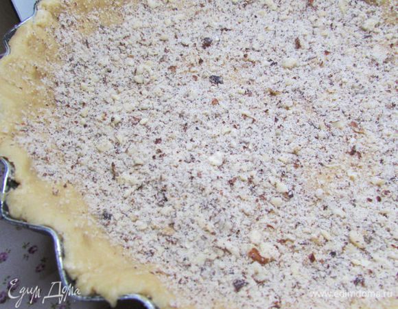 Охлажденное тесто разделите на две неравные части. 2/3 теста раскатайте на присыпанной мукой поверхности, затем покройте им дно формы и бортики на 3-4 см в высоту. Слегка присыпьте тесто молотым миндалем.