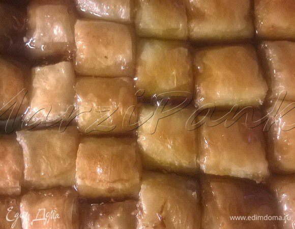 Готовую баклаву вынуть из духовки. Аккуратно придерживая подручными средствами содержимое формы, чтобы не соскользнуло, сливаем все масло в чашку (его можно будет использовать еще раз).

И сразу же поливаем холодным сиропом 