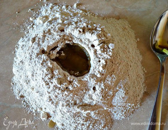 Для приготовления коржей просеять на стол по половине стакана ржаной и пшеничной муки, посолить. Сделать в центре муки лунку и влить в неё оливковое масло.