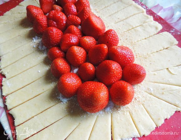Готовое тесто делим на две части, каждую раскатываем в прямоугольный пласт толщиной меньше сантиметра. По краям пласта острым ножом делаем надрезы шириной около 1,5 см и длинной 7-8 см. Середину каждого пласта посыпаем столовой ложкой белых молотых сухарей (можно воспользоваться панировочными, но попробуйте их, чтоб убедиться, что они не из ржаного хлеба). Высыпаем примерно 1/4 часть сахарно-крахмальной смеси и выкладываем клубнику носиками вверх.
