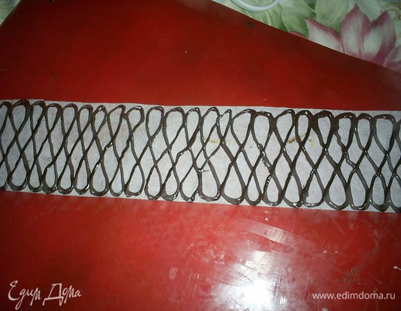 На этом этапе можно и остановиться. Просто посыпать поверхность торта какао через ситечко и подавать к столу. Торт настолько вкусный, что в украшениях он не нуждается. Но если время позволяет, то можно повозиться и с дополнительным декором. У меня был праздничный вариант и я решила сделать шоколадный бордюр вокруг торта. Для этого надо измерить высоту и длину окружности торта и вырезать из бумаги для выпечки прямоугольник подходящего размера. Его высота должна быть примерно на сантиметр больше высоты торта. Я побоялась рисовать на таком длинном кусочке и разделила его пополам. Далее рисуем растопленным шоколадом (у меня кондитерская глазурь в дисках) узор, какой душа пожелает. У меня рисунок был некрупный, мне понадобилось примерно 50 г шоколада (глазури).