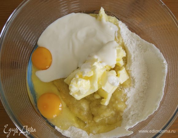 Духовку включить разогреваться на 180 С. 
Смешать в большой миске все сухие ингредиенты: просеять муку с разрыхлителем, пищевую соду, добавить сахар и щепотку соли. Размять крупный спелый банан и добавить к смеси сухих ингредиентов вместе с йогуртом, яйцами, размягченным сливочным маслом и ванилином (ванильной эссенцией).   