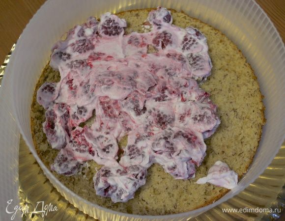 Начинаем промазывать торт. На блюдо установить разъемное кольцо. Положить первый корж и выложить на него сливки с малиной. Распределить равномерно по поверхности коржа.