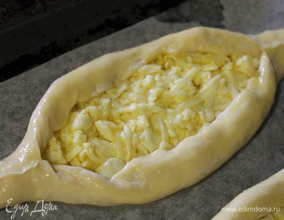 Завернуть края теста вверх, чтобы получились "лодочки". Переложить хачапури на застеленный пергаментом и смазанный маслом противень. Одно яйцо размешать в миске и смазать им бортики хачапури.