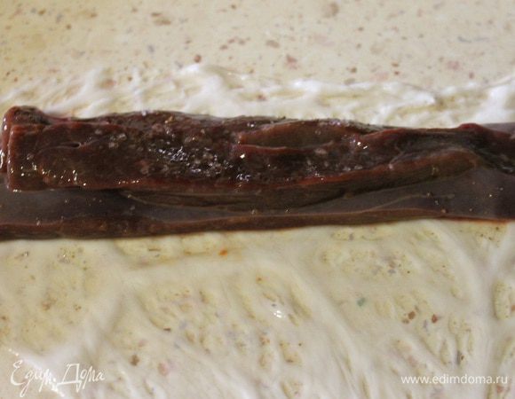 Берем жировую сетку, ее понадобится 30 г. Разрезаем ее на 3 части. Разравниваем каждую часть на рабочем столе и кладем ближе к длинному краю три брусочка печени. Солим, перчим по вкусу.