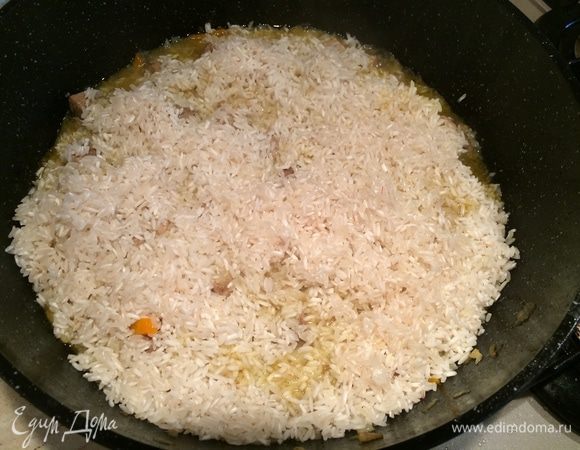 Через 30 минут всыпать рис и разровнять по поверхности мяса (не перемешивать). Залить горячей водой на 2 см выше риса. Накрыть крышкой, убавить огонь до минимума и томить до полного выпаривания жидкости.
Затем вдавить в рис чеснок (нечищеный), деревянной палочкой сделать отверстия для выхода пара. Готовить около 20 минут.
