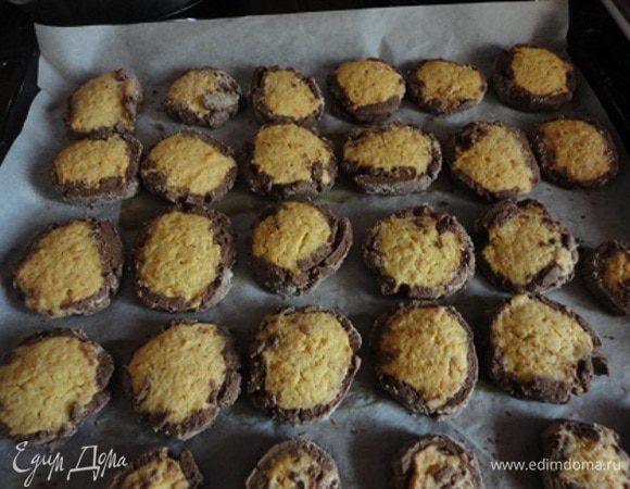 Нагреть духовку до 180 градусов. Рабочую поверхность посыпать кокосовой стружкой, смешанной с сахарной пудрой. Раскатать темное тесто в виде длинного прямоугольника толщиной 5 мм и слегка смочить его водой ! (я забыла это сделать, а напрасно). Сделать из светлого теста валик и закатать его в темное тесто. Нарезать кружочки толщиной около 1 см. Выпекать на выстланном бумагой противне 15 минут.