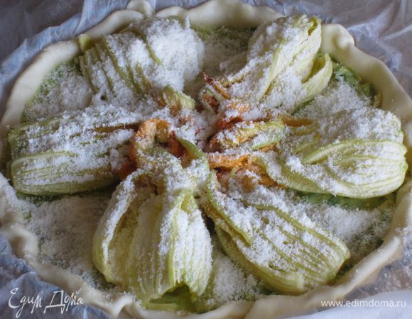 Слоёное тесто тонко раскатать, выложить в форму с пергаментом и наколоть вилкой. Выложить начинку, сверху разложить цветки цукини и посыпать оставшимся пармезаном.