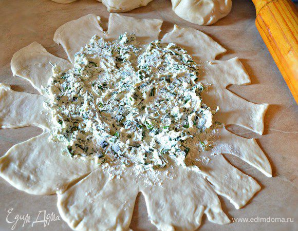 Руки и рабочую поверхность смазываем растительным маслом и раскатываем тесто тонко. Можно помочь руками, слегка растягивая тесто. В середину лепёшки кладём начинку, края надрезаем секторами.