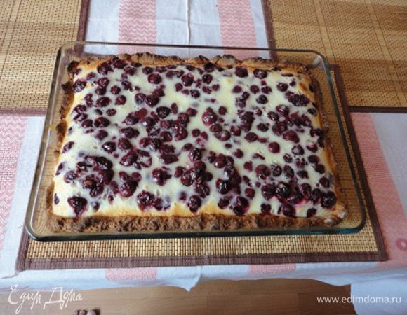 Вишню очистить от косточек и засыпать сахаром. Оставить примерно на 30 минут.
Приготовить тесто. Яйцо, сахар, ванильный сахар и соль взбить миксером. Добавить молоко, масло, творог и вновь перемешать миксером. Муку соединить с разрыхлителем, добавить к жидким ингредиентам и замесить тесто. Можно поместить в холодильник на время приготовления глазури.
Включить духовку для разогрева до 200 градусов. 
Приготовить глазурь. Яйца с сахаром взбить миксером до растворения сахара. Добавить сметану, крахмал и хорошо перемешать.
Противень смазать растительным маслом. Тесто раскатать и выложить в форму, образуя бортики, и посыпать сухарями.
С вишни слить образовавшийся сок и добавить в него сахарную пудру. Оставить его для смазки готового пирога. Ягоды без сока выложить на тесто и залить глазурью. Выпекать 30 минут.
