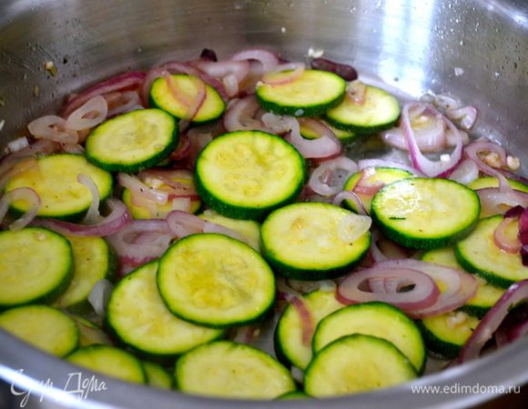 Тем временем для начинки нарезать кольцами лук, и цукини кружочками. В сковороде разогреть 1-2 ст.л. оливкового масла и положить лук, цукини, выдавить туда же 2-3 зубчика чеснока (по вкусу). Время от времени помешивая, дать овощам поджариться 5-6 минут. Они не должны зажариться, просто кабачок должен стать чуть мягче. Посолить и поперчить по вкусу. Выключить огонь и отставить в сторону. 
