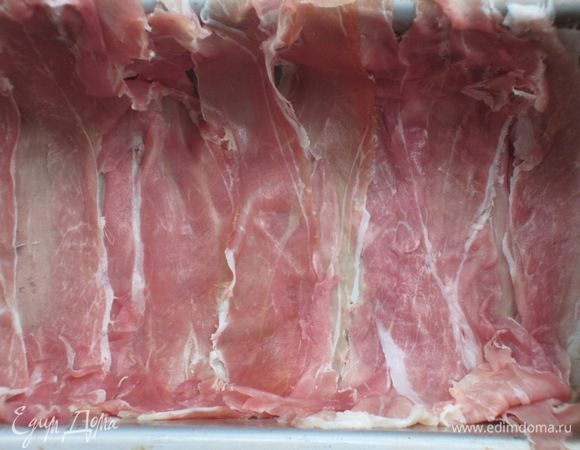 Смазанную оливковым маслом прямоугольную жаропрочную форму выложить тонкими ломтиками ветчины, укладывая их внахлест так, чтобы края свисали.