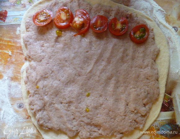 На тонко раскатанное тесто выложить тонким слоем фарш. На один край выложить порезанный помидор.