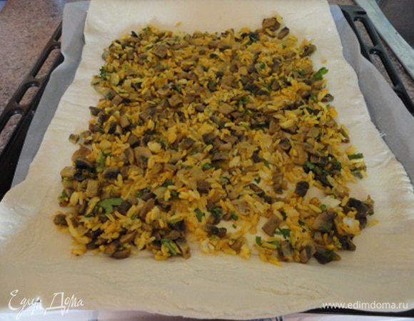 Рис отварить до готовности, воду слить. 
Лук нарезать мелкими кубиками, шампиньоны нарезать пластинами или кубиками и спассеровать на сливочном масле до золотистого цвета.
Лук, шампиньоны соединить с рисом и рубленной зеленью (вместо петрушки можно взять укроп, или все вместе - дело вкуса), посолить, поперчить по вкусу, приправить куркумой и хорошо перемешать.
Филе рыбы вымыть, обсушить и нарезать большими кусками. Я только отделила филе от кости и оставила целыми кусками. Филе посолить, поперчить по вкусу и полить соком лимона.
Тесто разморозить при комнатной температуре и раскатать в два прямоугольных листа. Я на двойную ному всех продуктов использовала три листа слоеного теста. Лист для выпекания выстлать бумагой и на него выложить один пласт теста. На него выложить половину начинки.