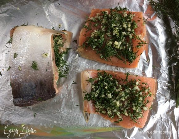 Возьмите лист фольги, смажьте совсем немного растительным маслом, положите на неё рыбу кожей вниз, сверху выложите зелень с чесноком и накройте второй половинкой филе.
