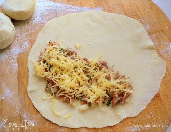 На одну сторону пласта положить 2 ст.ложки начинки, разровнять и посыпать сыром.