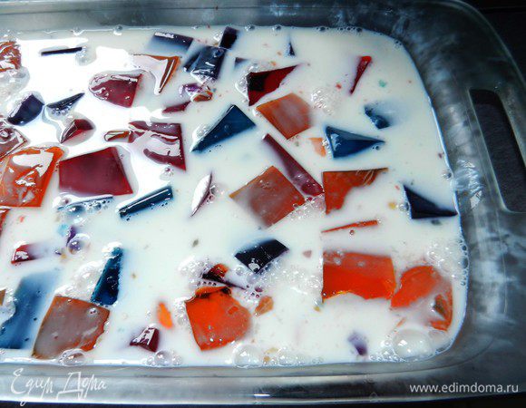 Достать из холодильника 4 разноцветных желе и порезать кубиками. Переложить в большую емкость, сбрызнутую спреем для выпечки, и залить смесью желе со сгущенным молоком. Охладить в холодильнике 2 часа или до полного застывания. 