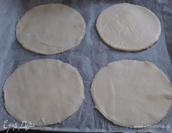 Слоёное тесто раскатать и вырезать 4 круга диаметром 10-12 см. Выложить тарталетки на противень с пергаментом.