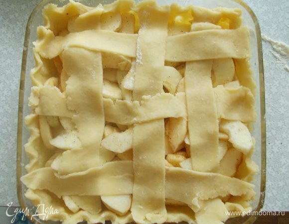 Оставшуюся треть теста раскатываем тонким слоем, режем полосками. Достаем форму из холодильника. Выкладываем яблоки и сверху выстилаем заранее подготовленные полоски теста, для украшения. 