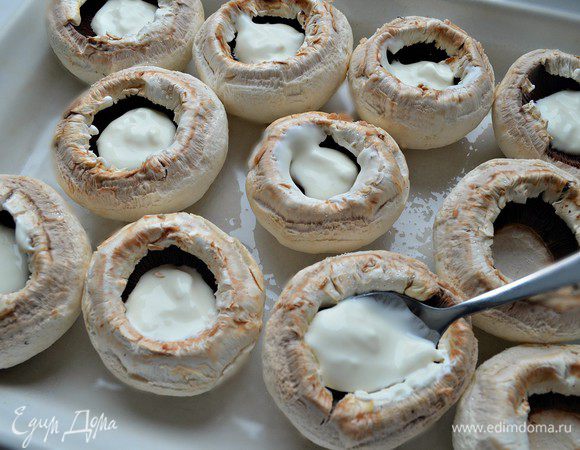Шляпки шампиньонов выложить на смазанный маслом противень. В каждую шляпку положить по 1 ч л сметаны, подсолить по вкусу и запекать в нагретой до 180 г духовке 7 мин.