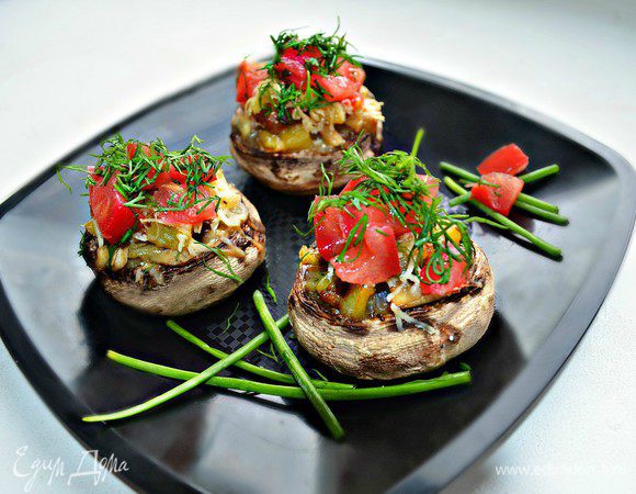 Наполнить шампиньоны приготовленной начинкой, посыпать натёртым сыром и запекать в нагретой до 180г духовке ещё 10-15 мин. Помидор нарезать мелкими кубиками, выложить поверх запечённых шампиньонов, посыпать нашинкованной зеленью, украсить зелёным луком и подать к столу. Приятного вам аппетита!