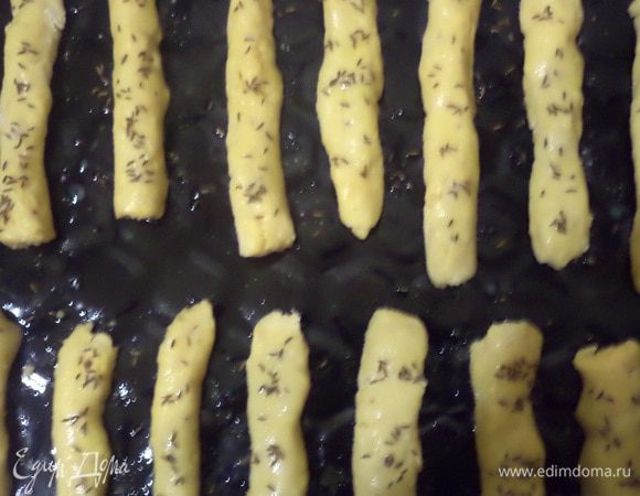 Скатать полоски в колбаски, выложить на смазанный маслом противень. 
Смазать взбитым яйцом, посыпать тмином и солью.
