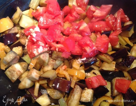 Помидор и чеснок добавьте к баклажанам. Посолите, поперчите, сделайте огонь тише и тушите под крышкой 5 минут. Выложите.