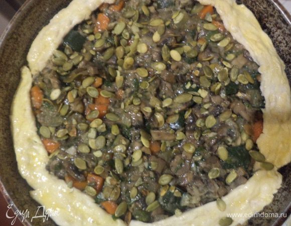 Круглую форму для выпечки смазать растительным маслом. Тесто разделить на две части: 3/4 и 1\4. Большую часть теста раскатать в круг, выстелить им форму, сформировав довольно высокий бортик. 
На тесто выложить начинку. Оставшееся тесто раскатать в тонкую полоску, выложить по краю сверху на начинку (серединка остаётся открытой).
По краю шов тщательно защипить. Сверху посыпать оставшимися тыквенными семечками.
Выпекать при температуре 190 градусов около 40 минут.