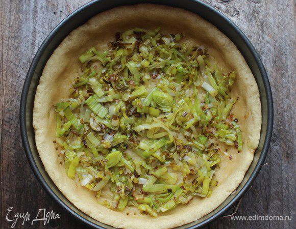 Пока тесто охлаждается, нарезать тонкими кольцами порей и обжарить его на оливковом масле до мягкости.  Охлажденный корж вынуть из холодильника, часто наколоть вилкой и выпекать в разогретой духовке 10–15 минут. Затем выложить на запеченный корж слой порея