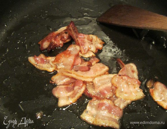 Полоски бекона нарезаем средне и обжариваем их на сухой сковороде до легкой корочки. Выкладываем их на бумажную салфетку, чтобы убрать лишний жир.
