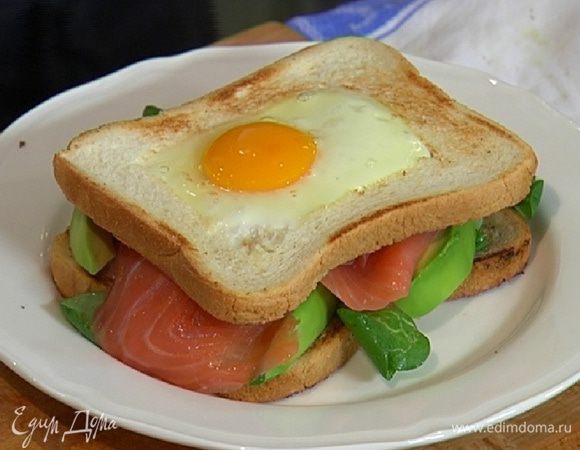 На обжаренный целый кусок хлеба выложить салат, ломтики авокадо, семгу и накрыть куском хлеба с яйцом.
