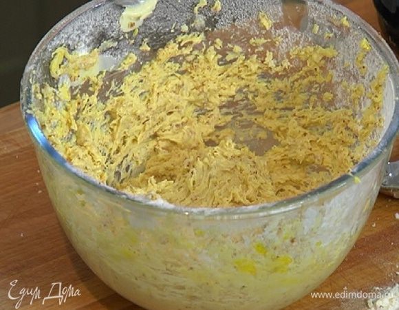 Убавить скорость и, не переставая взбивать, по одному ввести яйца, всыпать часть миндальной крошки и взбить еще немного.