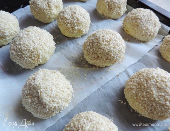 Подготовим противень. выстеленные бумагой для выпечки и емкость с холодной водой.
Делим наше тесто на 16 частей. Смачиваем руки водой и формируем круглые булочки. Каждую обкатываем в кунжуте.