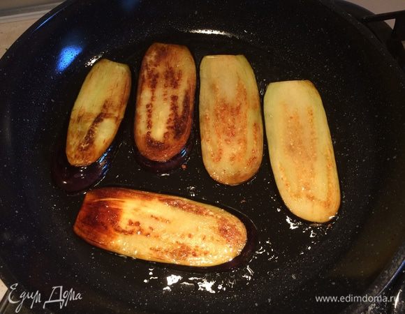 Баклажаны помыть, порезать вдоль на полоски толщиной 1-1,5 см, посолить и оставить на 30 мин. Затем обжарить баклажаны на растительном масле с двух сторон до золотистого цвета, выложить на бумажные салфетки и дать впитаться лишнему маслу.