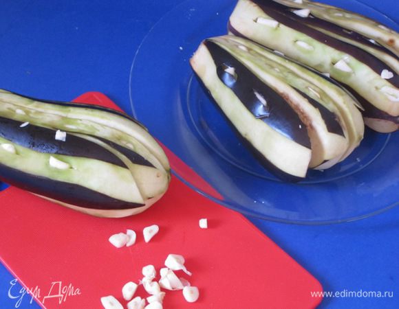 Промыть холодной водой от соли, просушить бумажным полотенцем. Нарезать чеснок пластинками. В баклажанах сделать надрезы. В надрезы вставить пластинки чеснока.