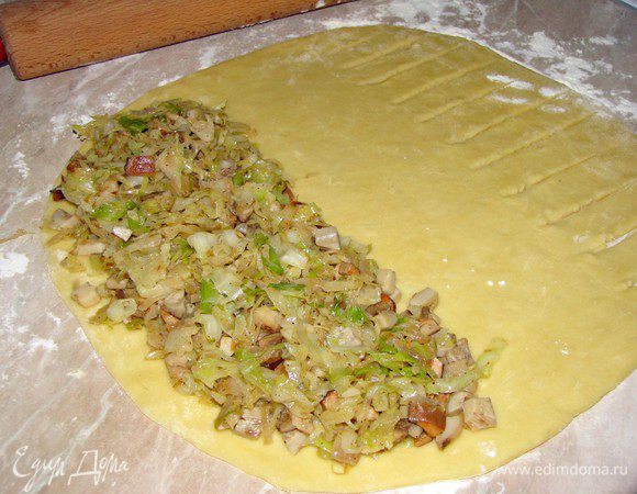 Тесто раскатать в прямоугольный пласт, оно очень мягкое и податливое. По краю выложить начинку. На другом краю теста острым ножом сделать прорези, не доходя до края.