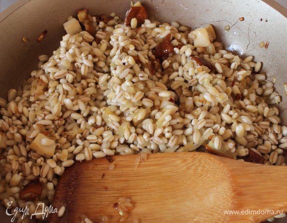 Добавить крупу к грибам и слегка обжарить. Затем влить вино и дать ему полностью выпариться. Необходимо постоянно мешать крупу ложкой или лопаткой.