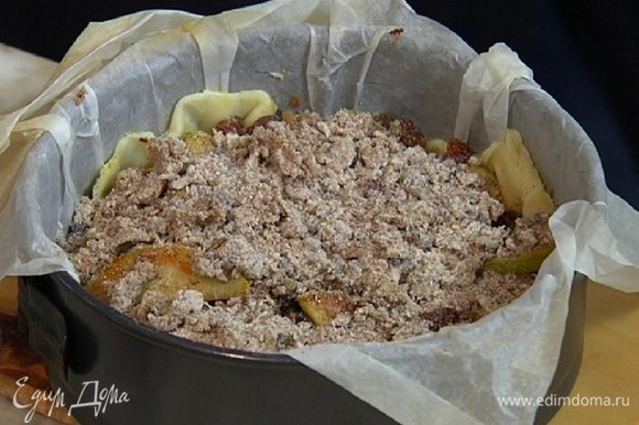 Вынуть песочный корж из духовки, удалить горох с бумагой, равномерно разложить фрукты с изюмом и посыпать сверху засыпкой.