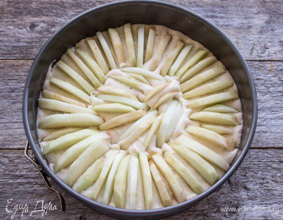 Белки взбить до крепких пиков, соединить с основной массой и аккуратно перемешать. Полученную массу выложить в форму для выпечки, выстеленную пергаментом. Яблоки очистить, освободить от семян и кожицы, нарезать тонкими дольками. Воткнуть в тесто по кругу выпуклой стороной вверх, плотно друг к другу по всей поверхности пирога. 
