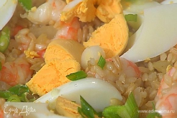 Выложить рис с креветками на блюдо, украсить нарезанными яйцами и луком.