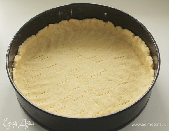Раскатать тесто скалкой. Выложить тесто в форму диаметром 26–27 см, сделать бортики высотой не менее 2 см. Наколоть тесто вилкой и убрать форму с тестом на 30 минут в холодильник. Выпекать 15 минут в духовке, предварительно разогретой до 180°C.