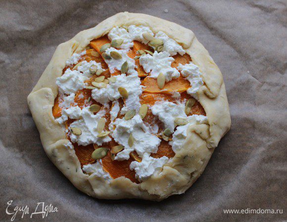 Края теста завернуть, сформировать бортики. Яйцо слегка взбить, смазать тесто кистью. Остатки яйца смешать со сливками и залить пирог. Сверху посыпать тыквенными семечками. 