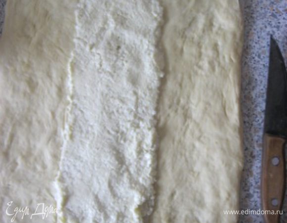 Подошедшее тесто обмять и раскатать в прямоугольник - 30х40 см.
Сразу переложить пласт на пергаментную  бумагу.
Визуально разделить пласт вдоль на три части.
На среднюю часть распределить сливочную начинку, оставив сверху и снизу по 2 см.