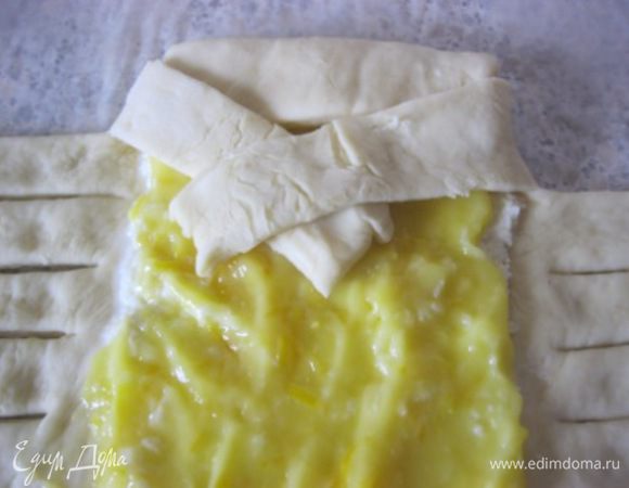Верхний клапан теста загнуть, закрывая начинку.
Начать плести косу, для этого поднять одну полоску теста и аккуратно загнуть ее по диагонали через начинку, также повторить и с другой стороны.