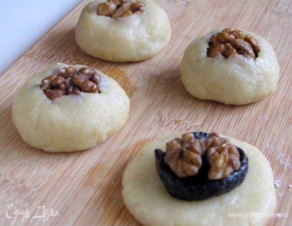 Расплющить шарик теста в аккуратную лепешечку, выложить чернослив, затем половинку грецкого ореха. Подвернуть края теста так, чтобы выглядывал орешек.