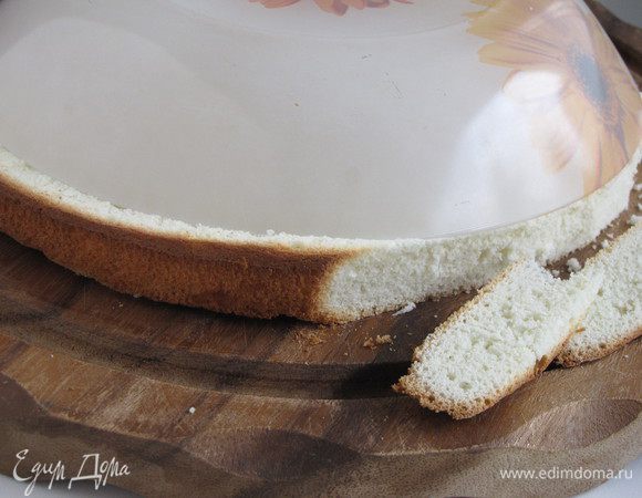 Далее бисквит необходимо уменьшить в диаметре. Для этого положить на него тарелку меньшего диаметра и острым ножом обрезать лишнее. Можно так же подровнять бисквит сверху, сделав его чуть тоньше. 