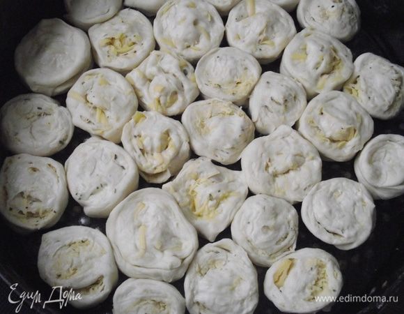 Присыпать поверхность стола мукой. Раскатать тесто толщиной в 1 см, натереть сверху сыр, посыпать травами, цедрой лимона и «сбрызнуть» небольшим количеством оливкового масла. Свернуть тесто в рулет и разрезать на равные части. Уложить «розочки» в форму, оставляя промежуток между ними. Тесто подойдет и заполнит всю форму.