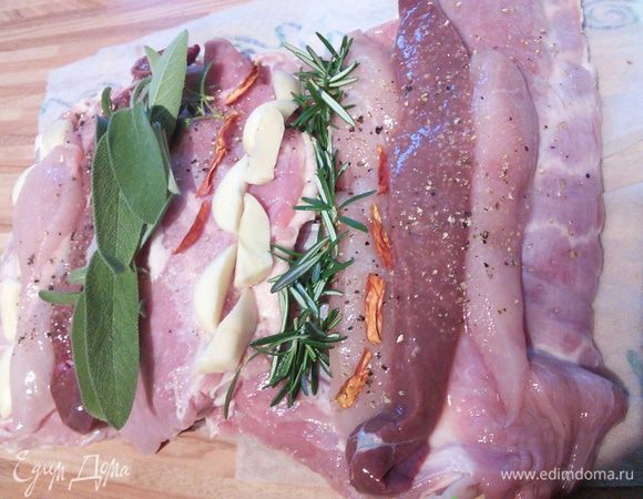 Мясо я купила уже запакованное в чулок. Когда делаю простую буженину, проделываю ножом дырки и шпигую мясо с разных сторон. Тут задача усложнилась и мне пришлось чулок для начала снять. Мясо распластала по столу, это брюшко поросёнка. Разложила куриную грудку, порезав ее вдоль на 2 части, так же печенку, сняла иголочки с розмарина, выложила в ряд, так же поступила с шалфеем (его можно заменить на лавровый лист), чеснок порезала на части, из него сделала 2 рядка, т. ж. перчик чили. Хорошенько посолила и поперчила. 