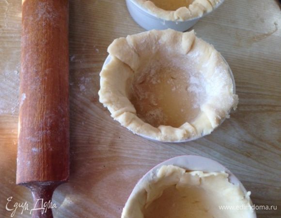 Охлажденное тесто разделить на части из расчета на три керамические формочки (на каждую формочку причитается основа + "крышечка" из теста). Раскатать каждую часть большим диаметром, чем формочка, присыпая поверхность и скалку мукой, выложить в формочки, сформировав высокие бортики с "запасом".