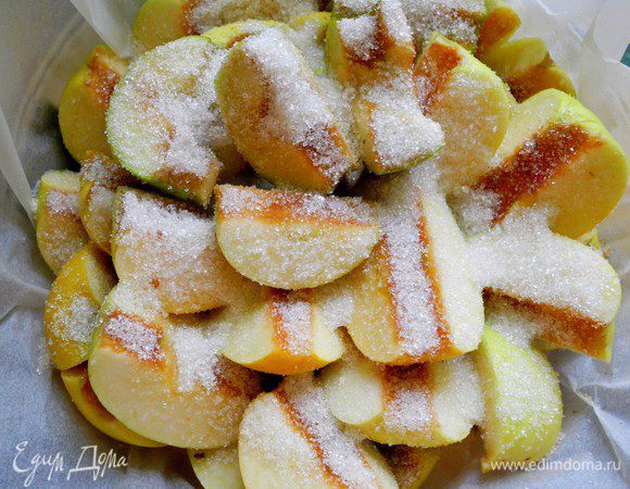 Сначала подготовим яблоки. Яблоки в исходном рецепте рекомендуются именно антоновские.  Нарезаем их на четвертинки, удаляем сердцевину.
Возьмем форму 26 см. Если есть чугунная сковородка с высокими бортиками, будет отлично. У меня форма из жаропрочного стекла. Застилаем форму бумагой для выпечки, сверху раскладываем кусочки сливочного масла и посыпаем половиной стакана сахара. Сверху плотно укладываем яблоки. Получается 2 слоя. Сверху снова посыпаем сахаром (полстакана). 